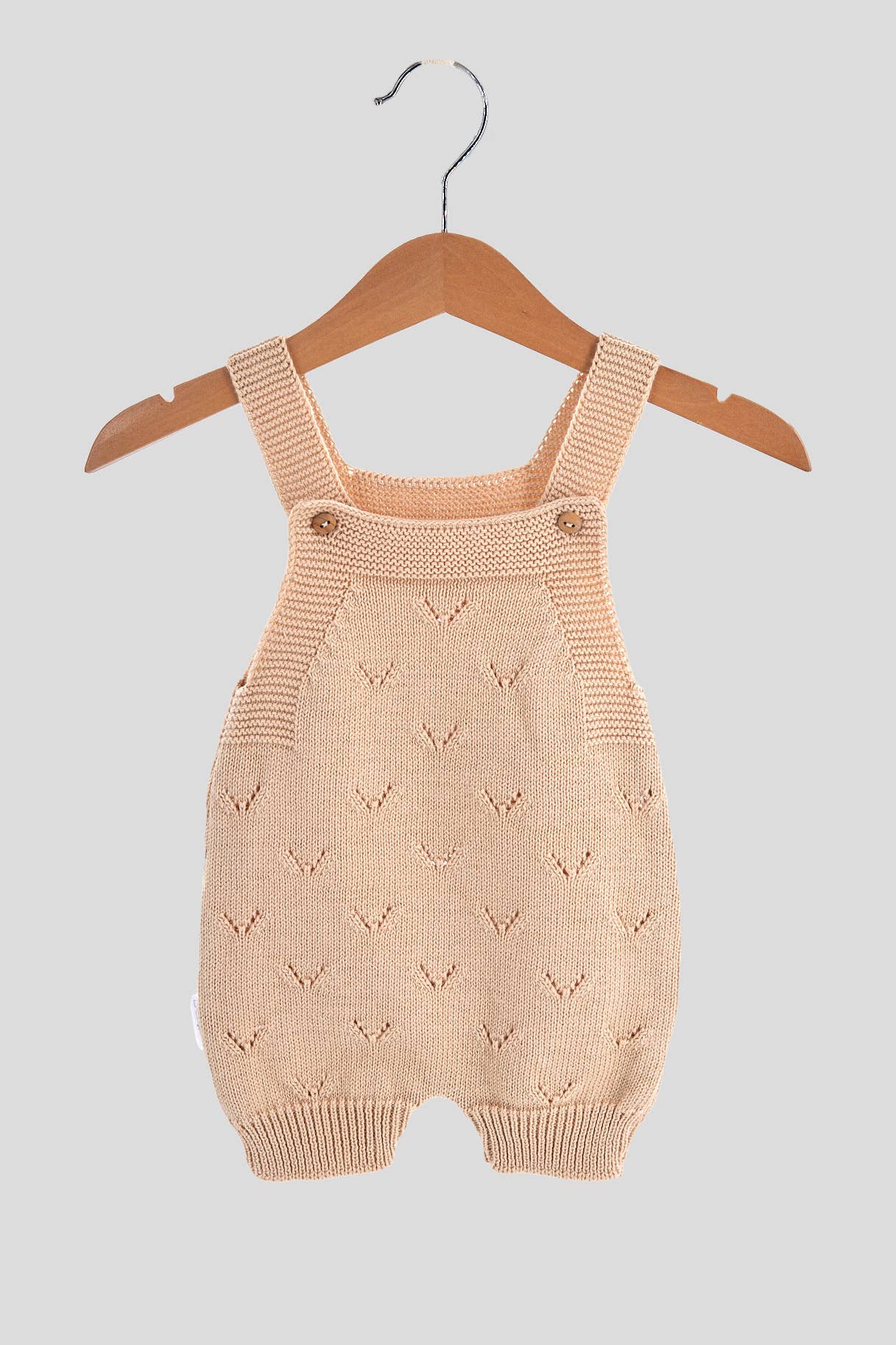 Knit jumpsuit in soft peach color, featuring V pattern, suitable for infants 1-3M and 3-6M, hangs on wooden hanger.