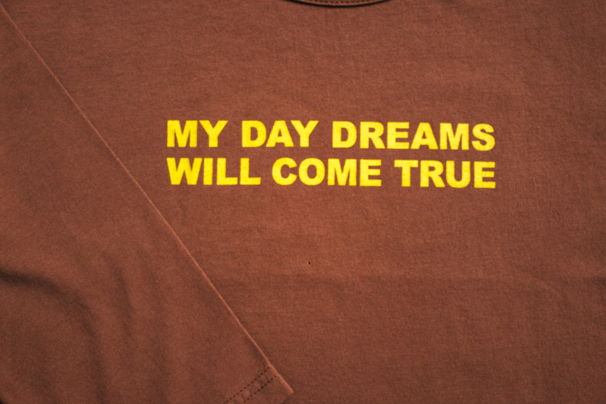 Chocolate long-sleeve tee featuring "My Day Dreams Will Come True" in bold yellow text, part of the Every.Body selection for kids.