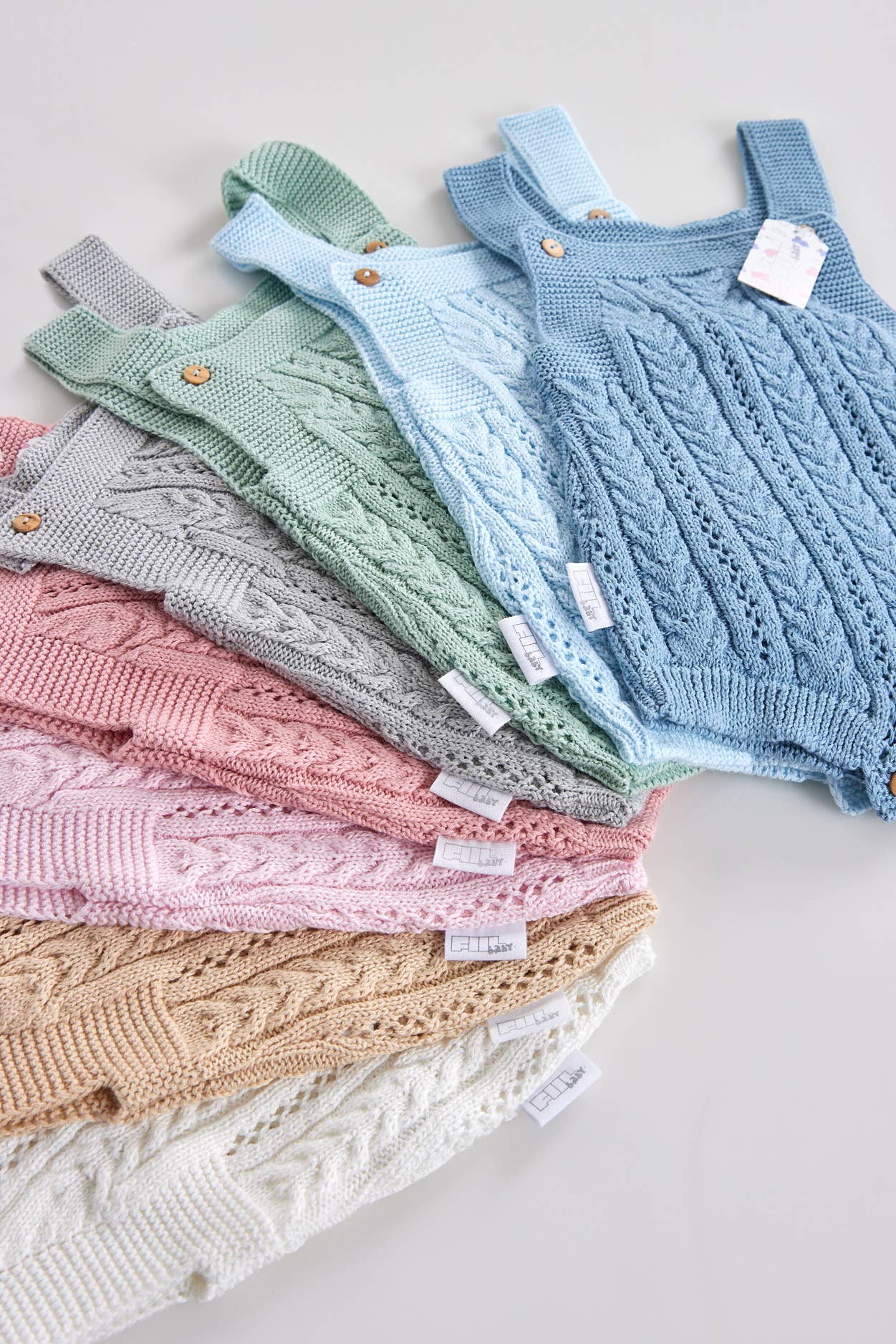 Soft cotton knit rompers in assorted colors: pearl, sand, pink, gray, green, and blue, inspired by nature and sustainability.