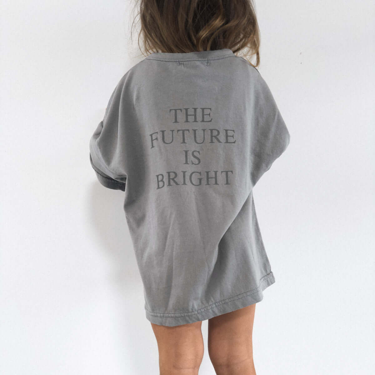 Child wearing oversized gray shirt with "The Future is Bright" text, symbolizing optimism in sustainable kids' fashion.