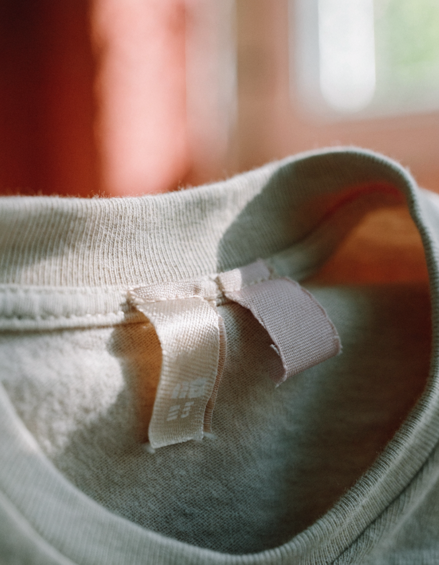 Close-up of a woven care label and fibre composition tag inside a beige organic cotton children's t-shirt