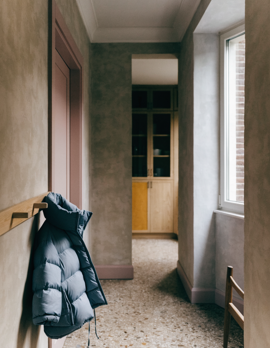 A child's winter coat hanging on a wooden peg rail in a calm minimal hallway