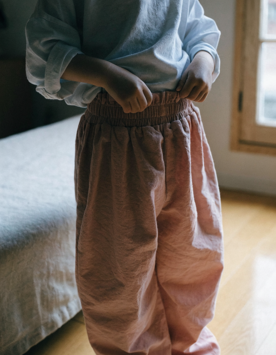 A toddler's hands pulling up soft organic cotton trousers with a wide elastic waistband
