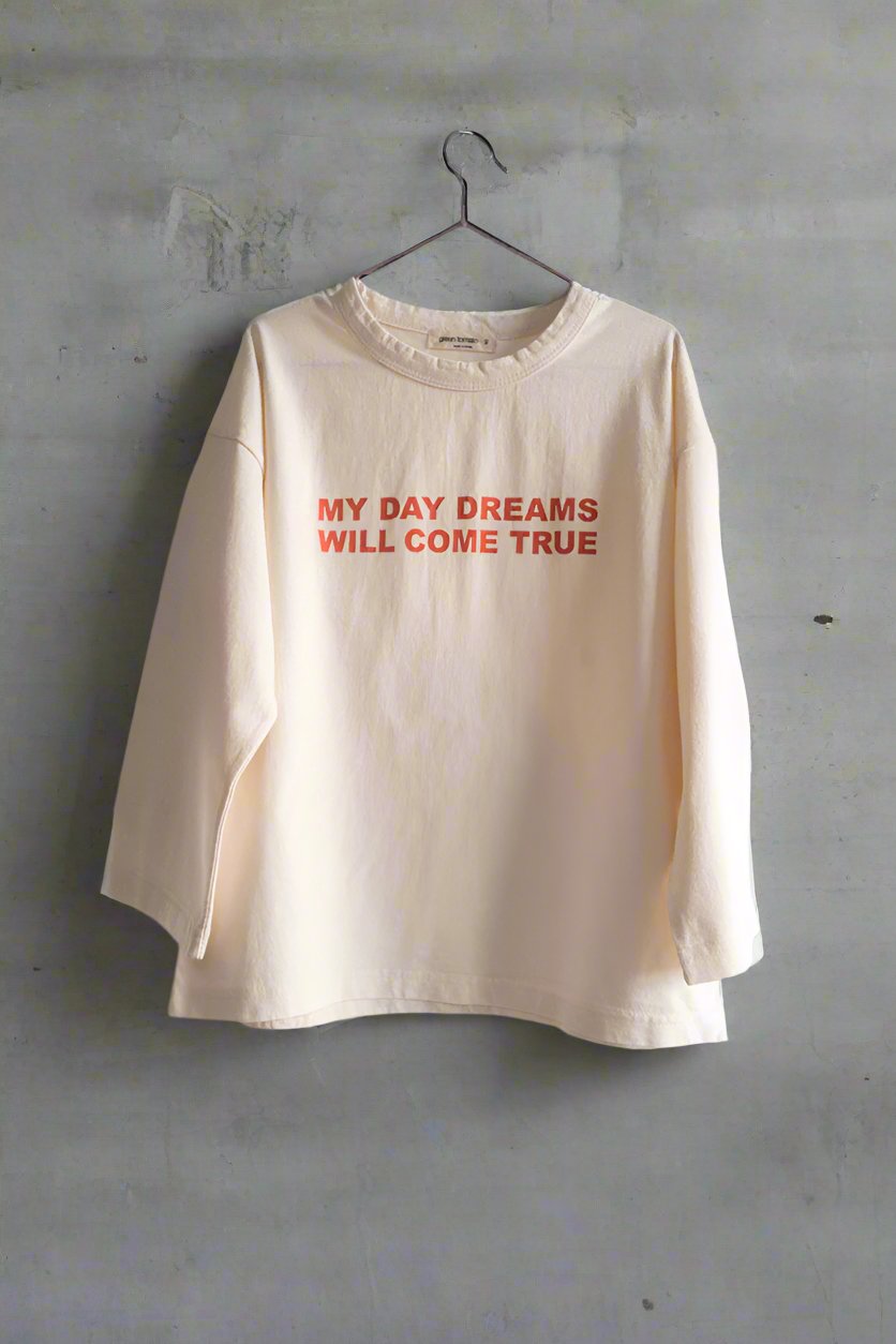 Ivory long-sleeve tee with &quot;My Day Dreams Will Come True&quot; print, loose fit, part of Every.Body selection, hangs on hanger against gray wall.